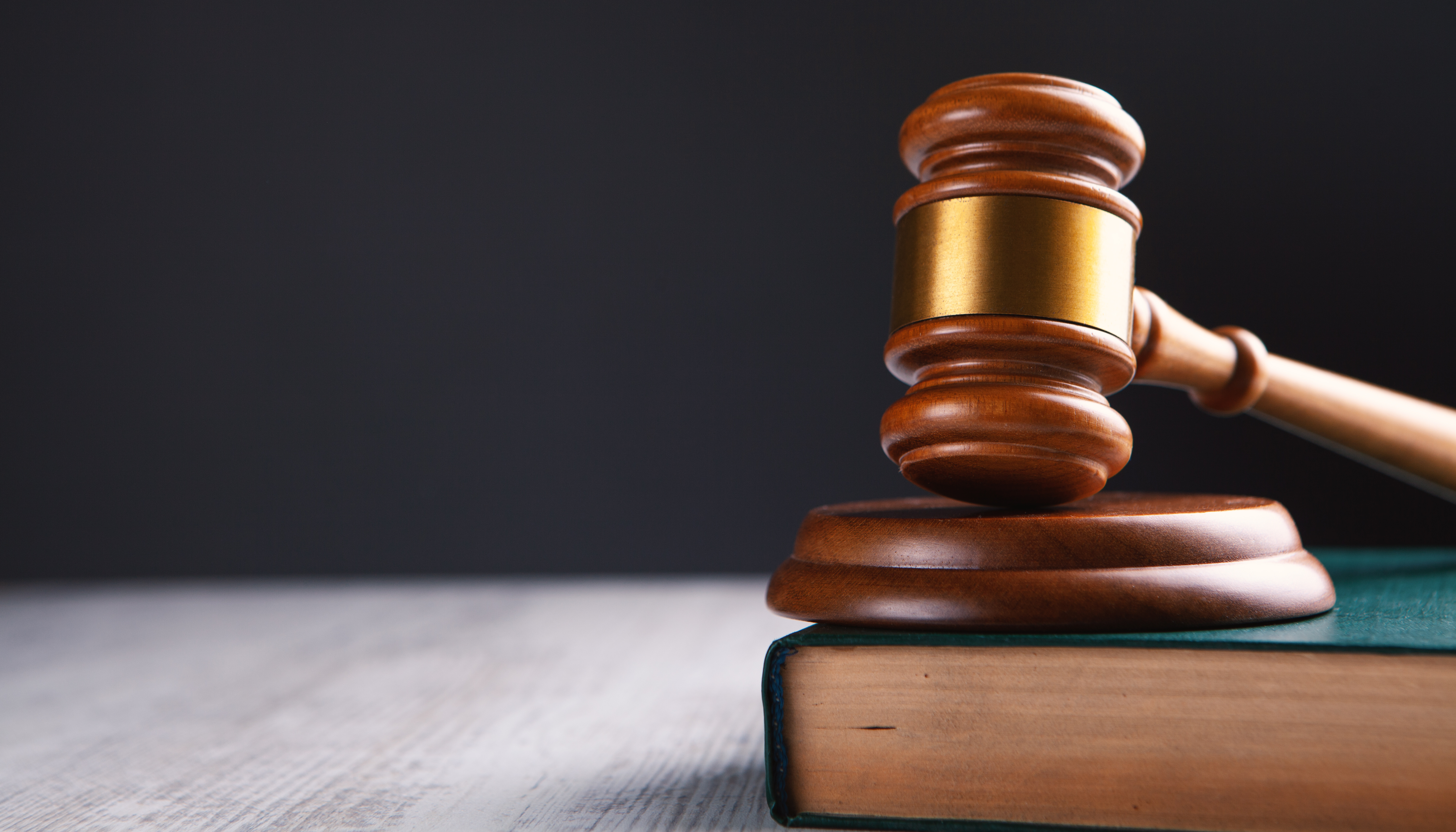 A wooden gavel rests on top of a green book on a wooden desk.