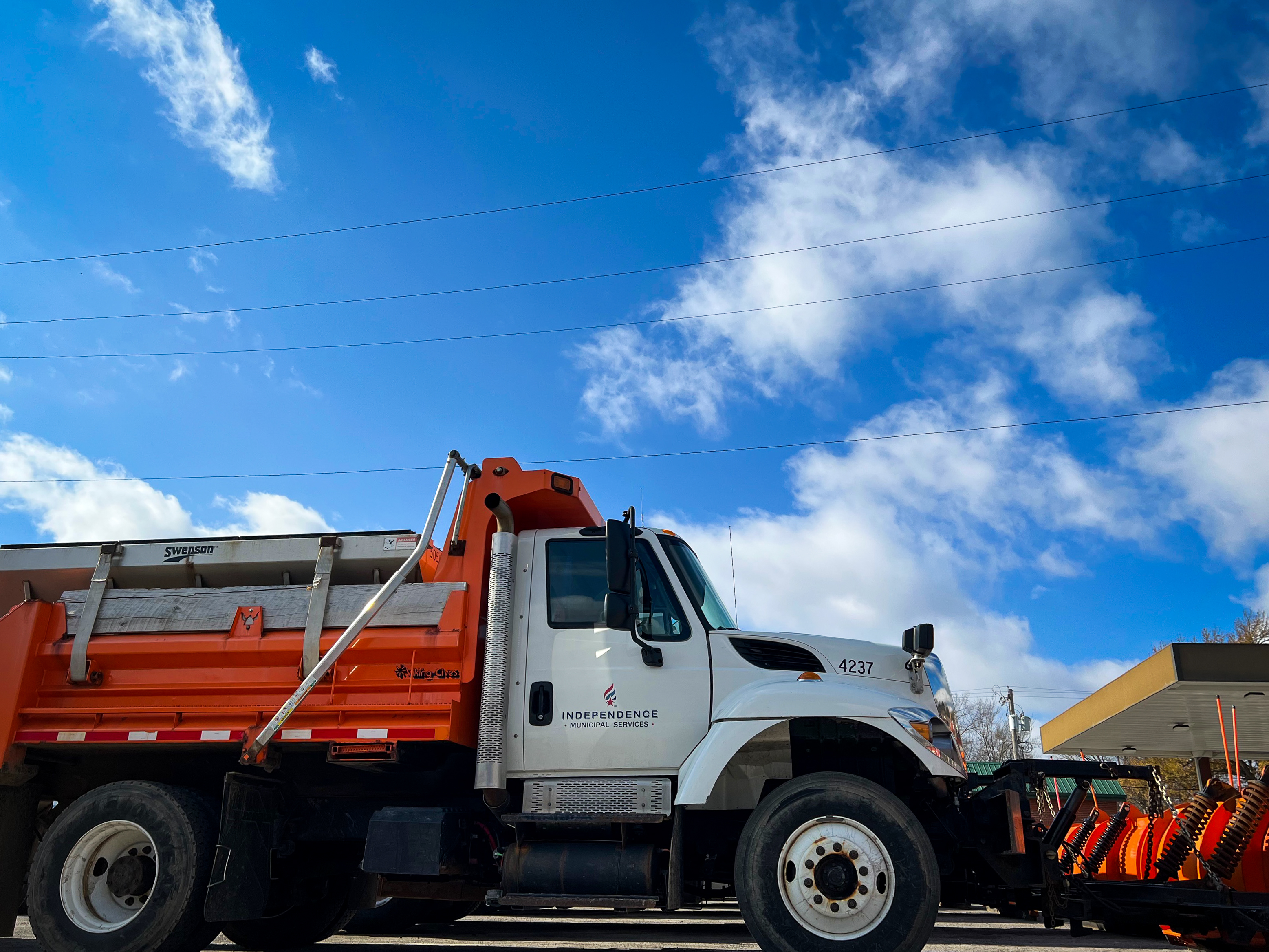 A snow plow with a bright orange shove on the front is lit from behind by the sun