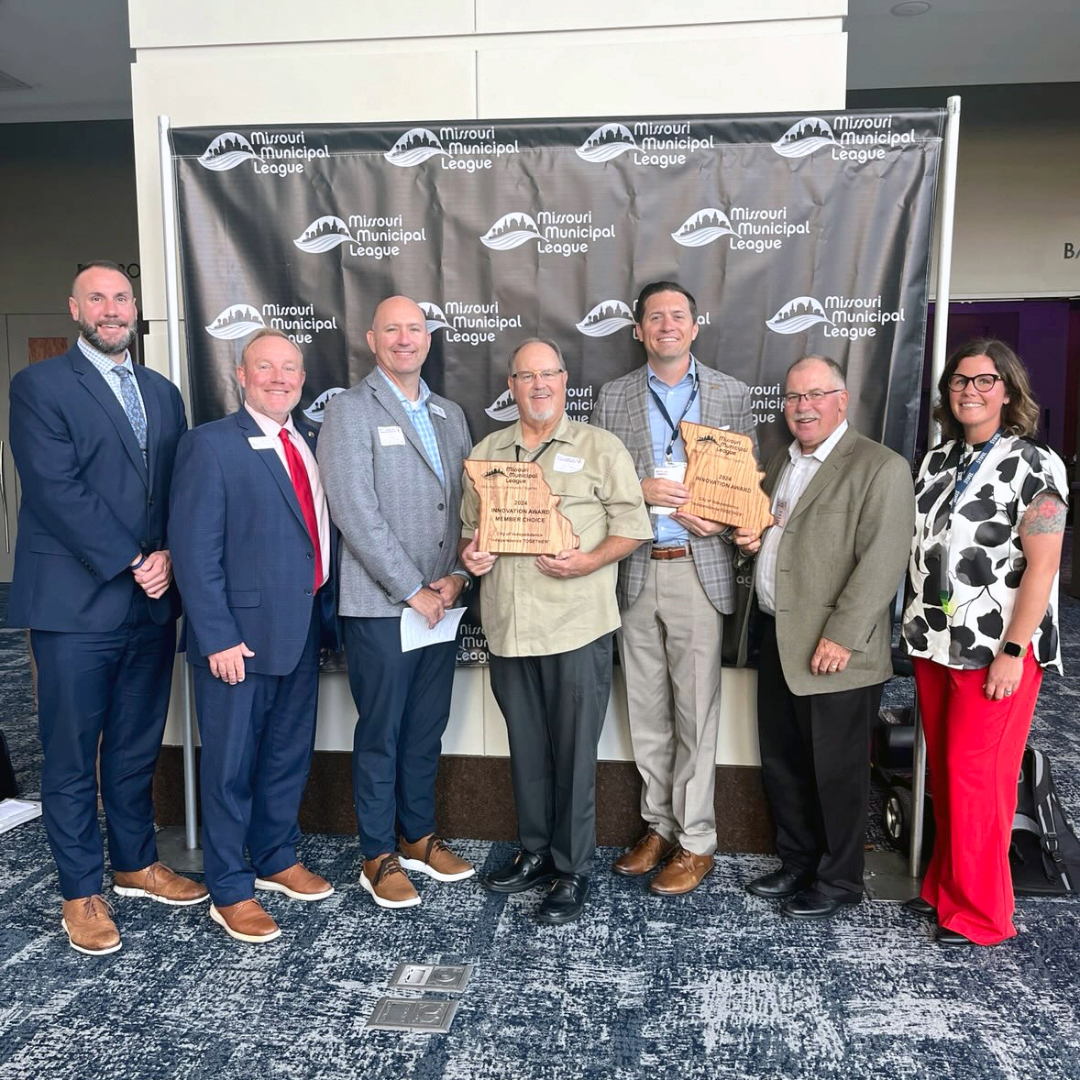 Seven people stand shoulder to shoulder; two hold awards in the shape of Missouri.