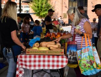 Farmers' Market patrons shop from a vendor in the outdoor area of the Uptown Market. 