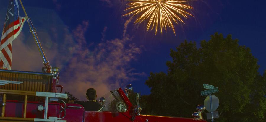 Image of a firetruck with person watching fireworks in sky