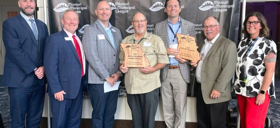 Seven people stand shoulder to shoulder; two hold awards in the shape of Missouri.