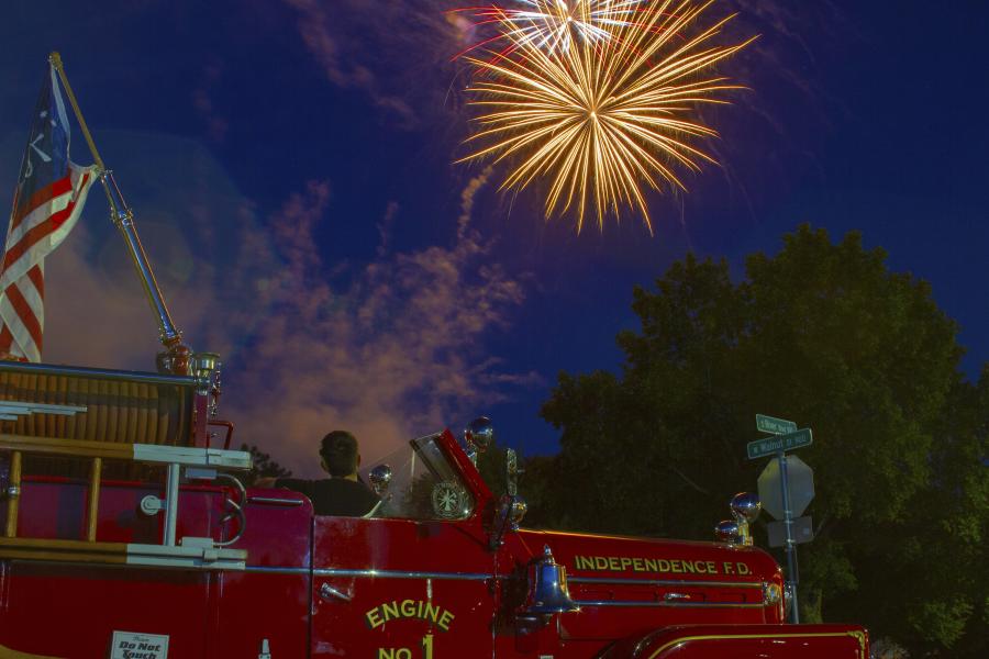 Image of a firetruck with person watching fireworks in sky