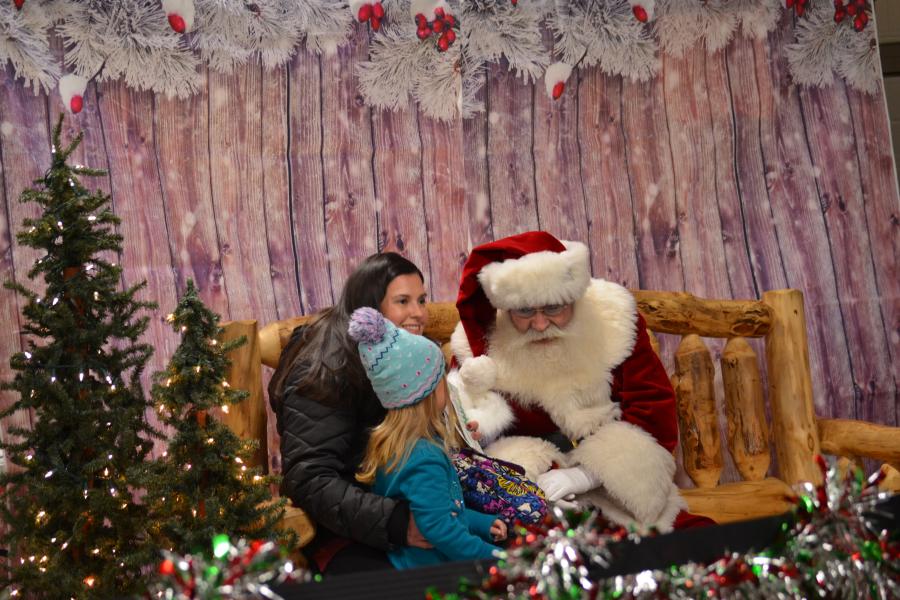 Photo of Santa, a little girl and parent at Santa's Village a holiday event held at the Independence Uptown market.