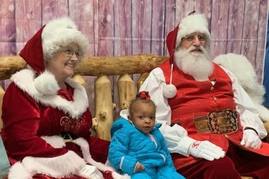 Santa and Mrs. Claus joined by a young child on a wooden bench