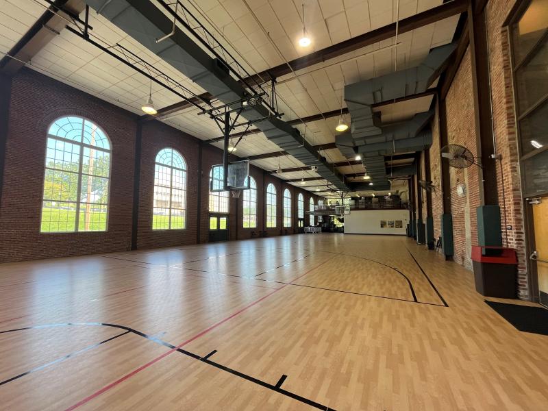 An image of an empty gymnasium space looking North with large windows and brick walls inside the Sermon Center.