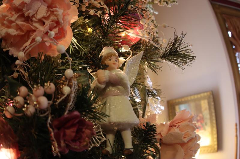 Image of a tree with angel ornament and pink roses. Inside the Vaile Mansion.