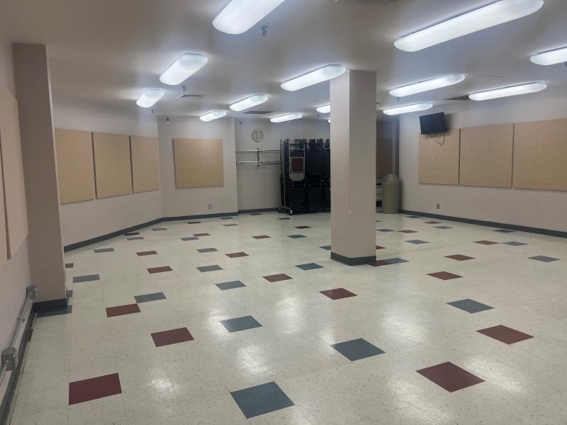 An image of inside the South Meeting Room at the Sermon Center with stacking folding chairs against a wall, bright lights, sound boards on the walls, and colorful square tiles on the floor.