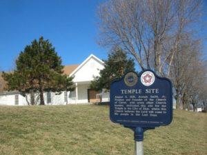 An exterior view of the site where the original temple lot dedicated by Joseph Smith is located. Picture includes a building and historic marker.